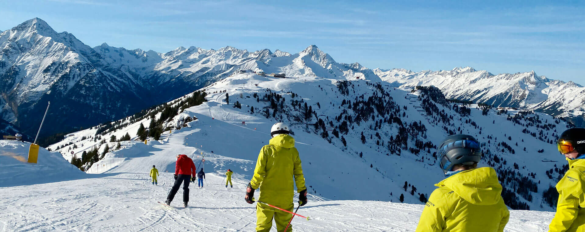 Mehrere Skifahre fahren gemütlich entlang, im Hintergrund eine Bergkulisse